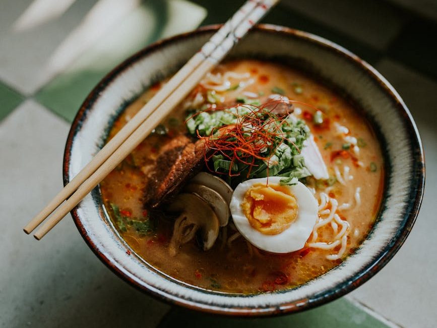 A bowl of ramen topped with slices of meat, green onions, and a boiled egg, with chopsticks resting on the rim.