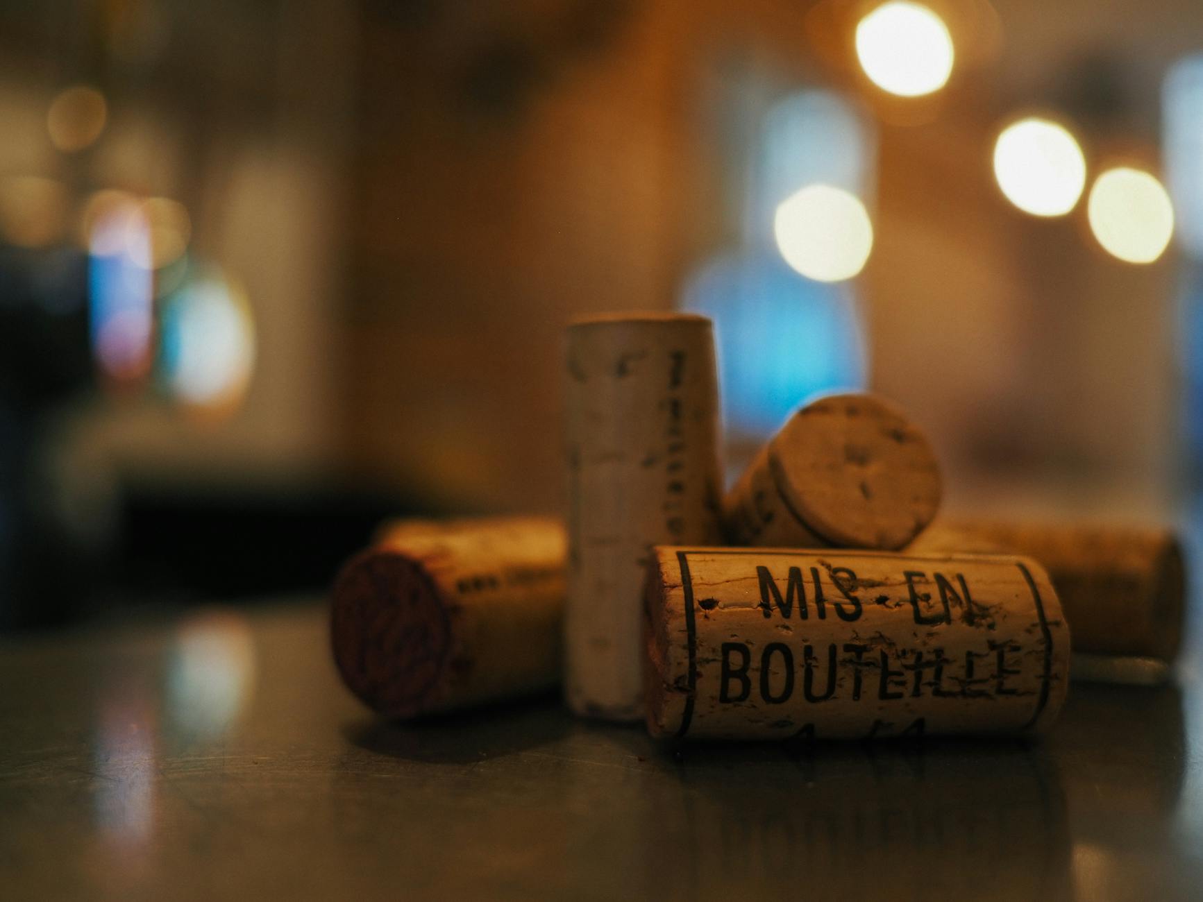 A collection of wine corks on a reflective surface, with warm bokeh lights in the background.