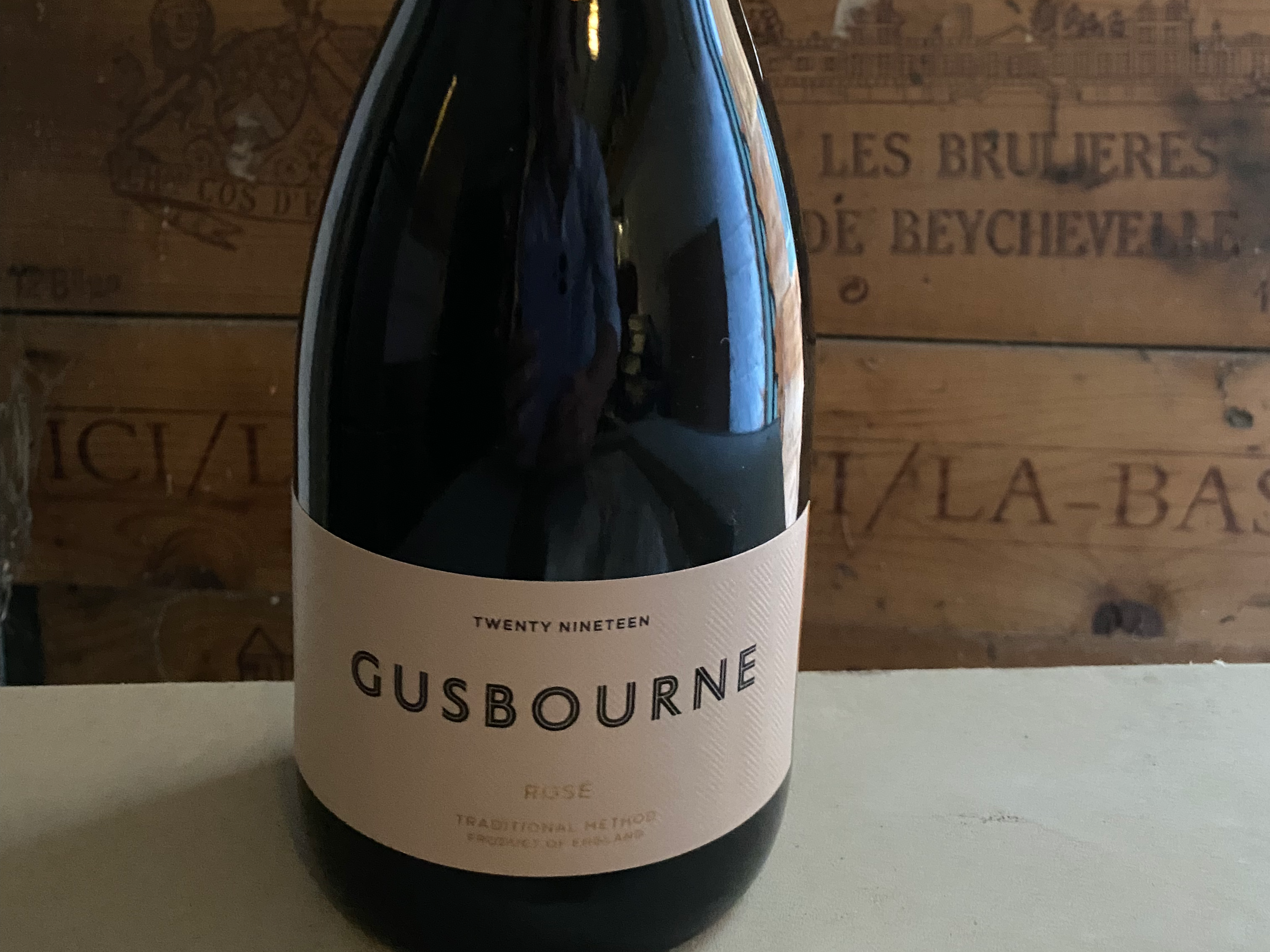 A bottle of Gusbourne Rosé sparkling wine with a pink label, displayed against a wooden backdrop with vintage wine crates.