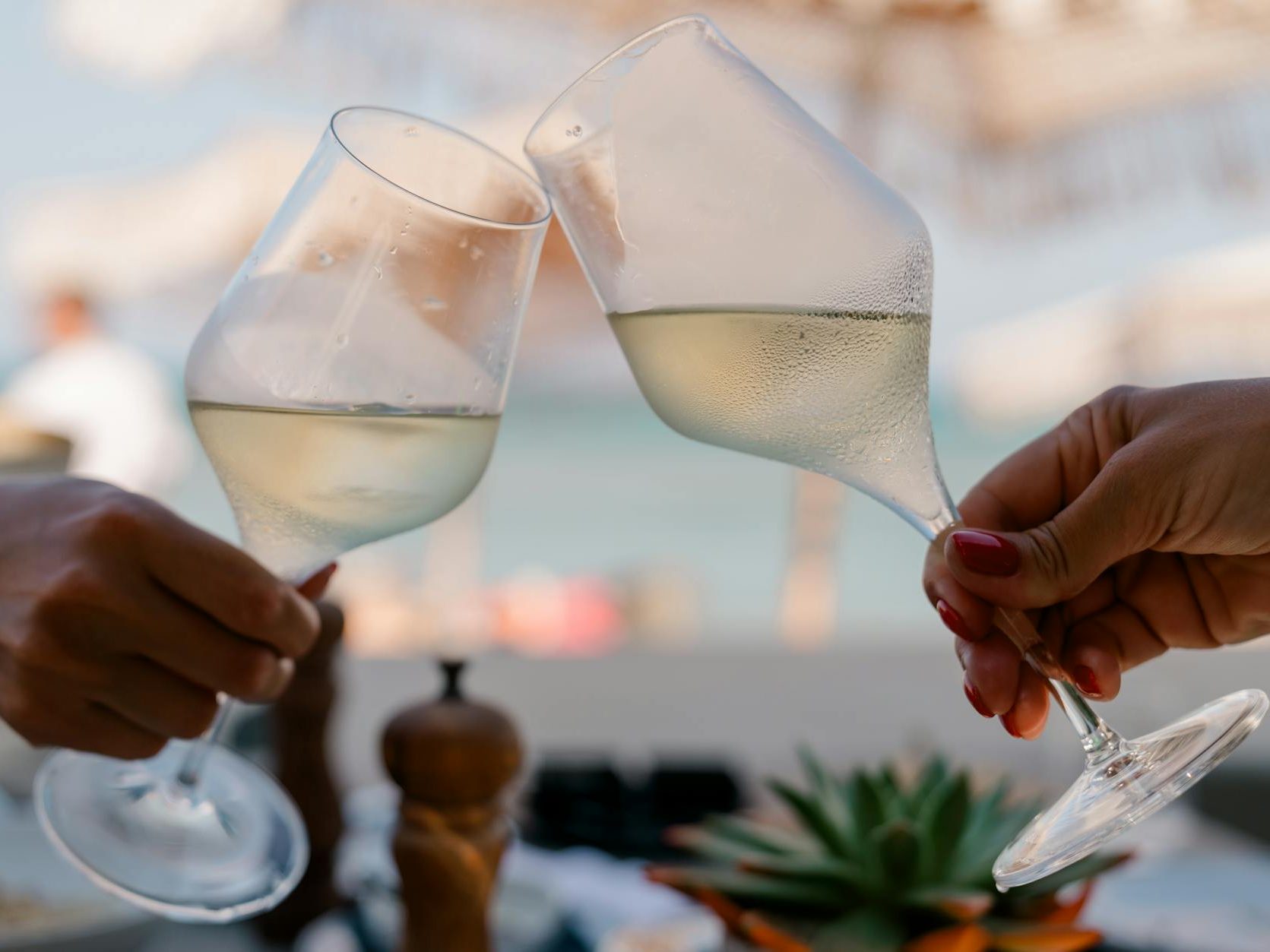 Two glasses of sparkling wine clinking together in a celebratory toast, with a blurred background of a sunny outdoor setting.
