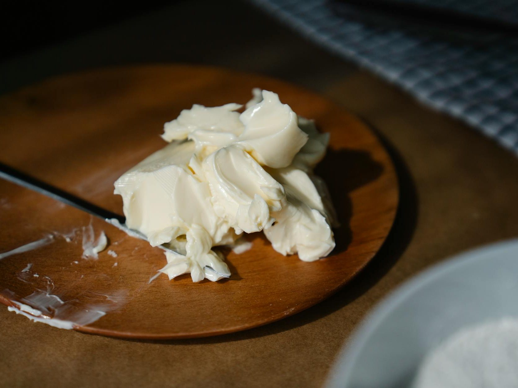 A wooden plate with a pile of butter and a knife beside it, set against a textured background.
