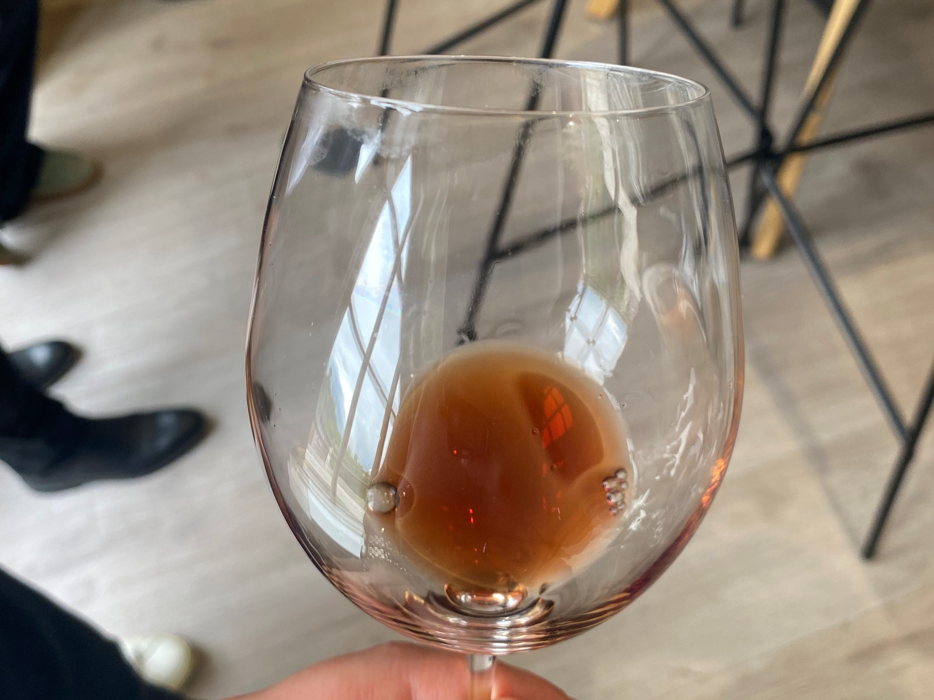 A hand holding a wine glass filled with a reddish-brown Chianti wine, reflecting light from a nearby window.