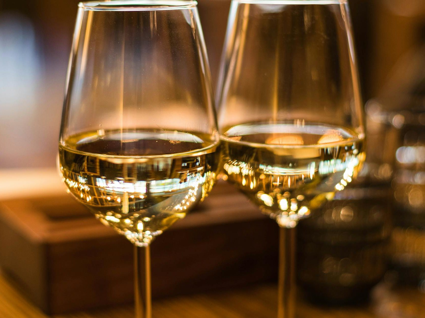 Two glasses of white wine, reflecting light, on a wooden table.